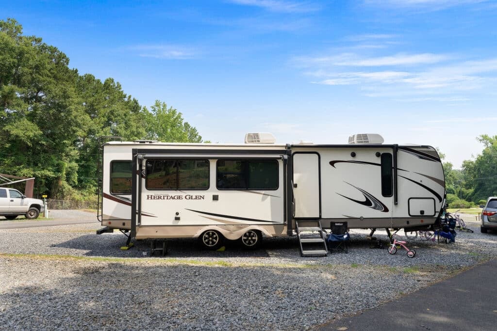 Large fifth-wheel RV parked at a gravel site.