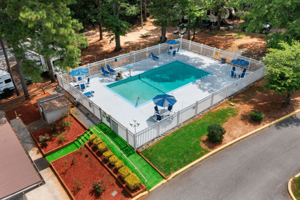 Forsyth Station RV Resort pool in Forsyth, GA, with lounge chairs, umbrellas, white fencing, and wooded RV sites.